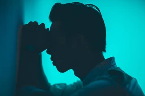 Image of a man in pain holding his head and leaning against a wall.